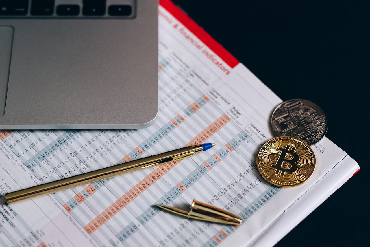 Flat lay of Bitcoin coins on a financial report with a laptop and pen.