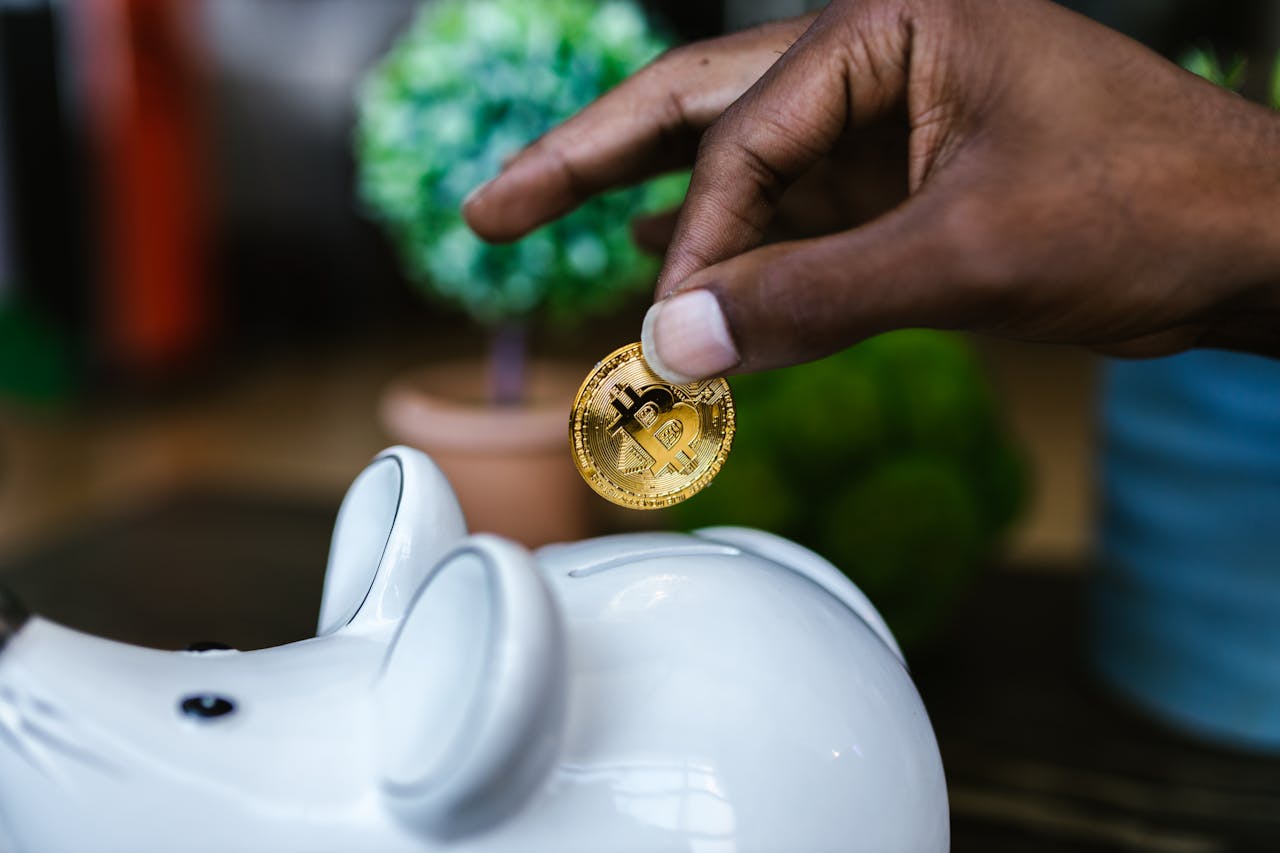 A close-up of a hand placing a bitcoin into a white piggy bank, symbolizing investment and savings.